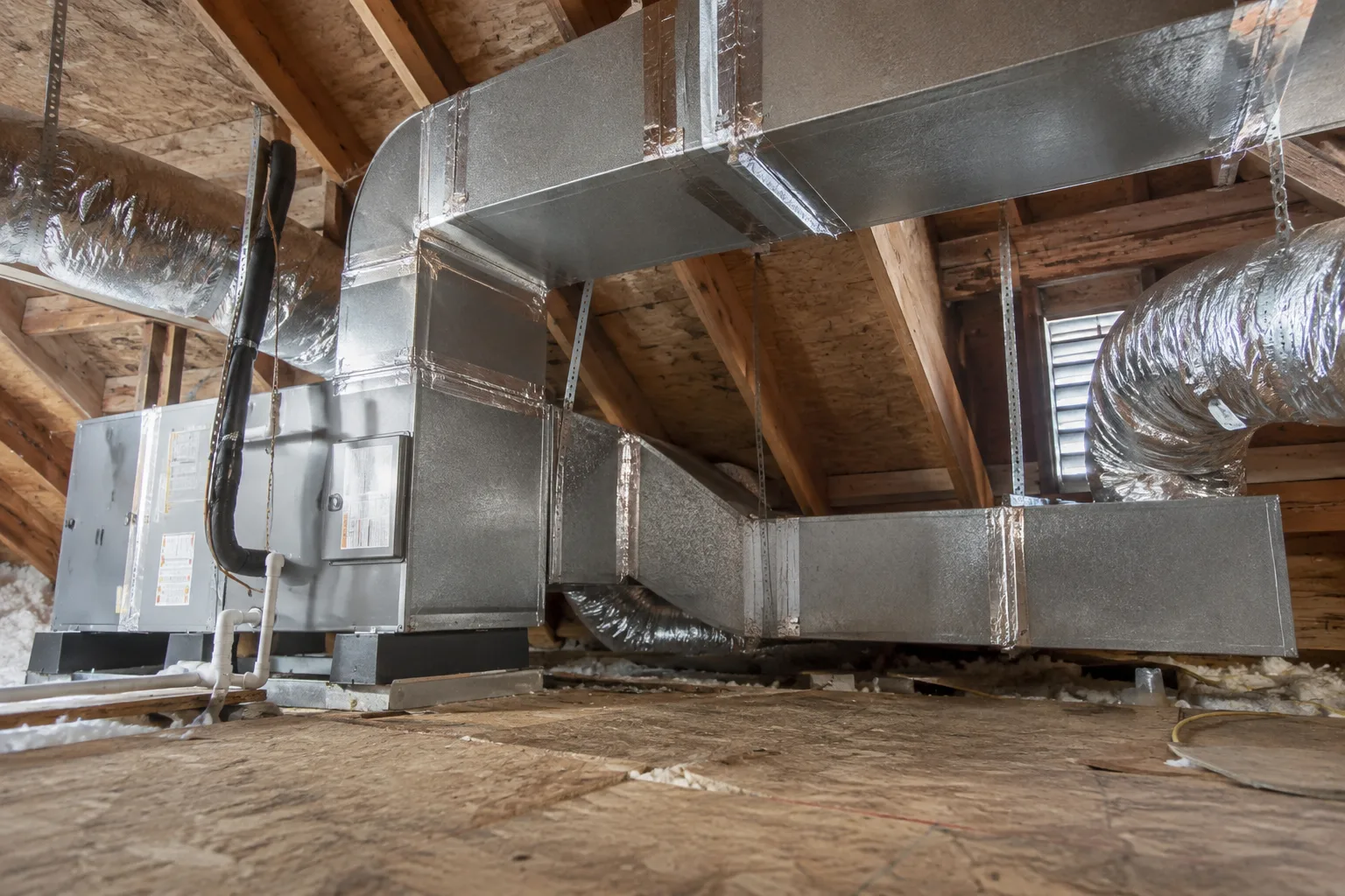 Newly installed attic air handler with a sheet-metal supply plenum and insulated ducts branching across the framing.